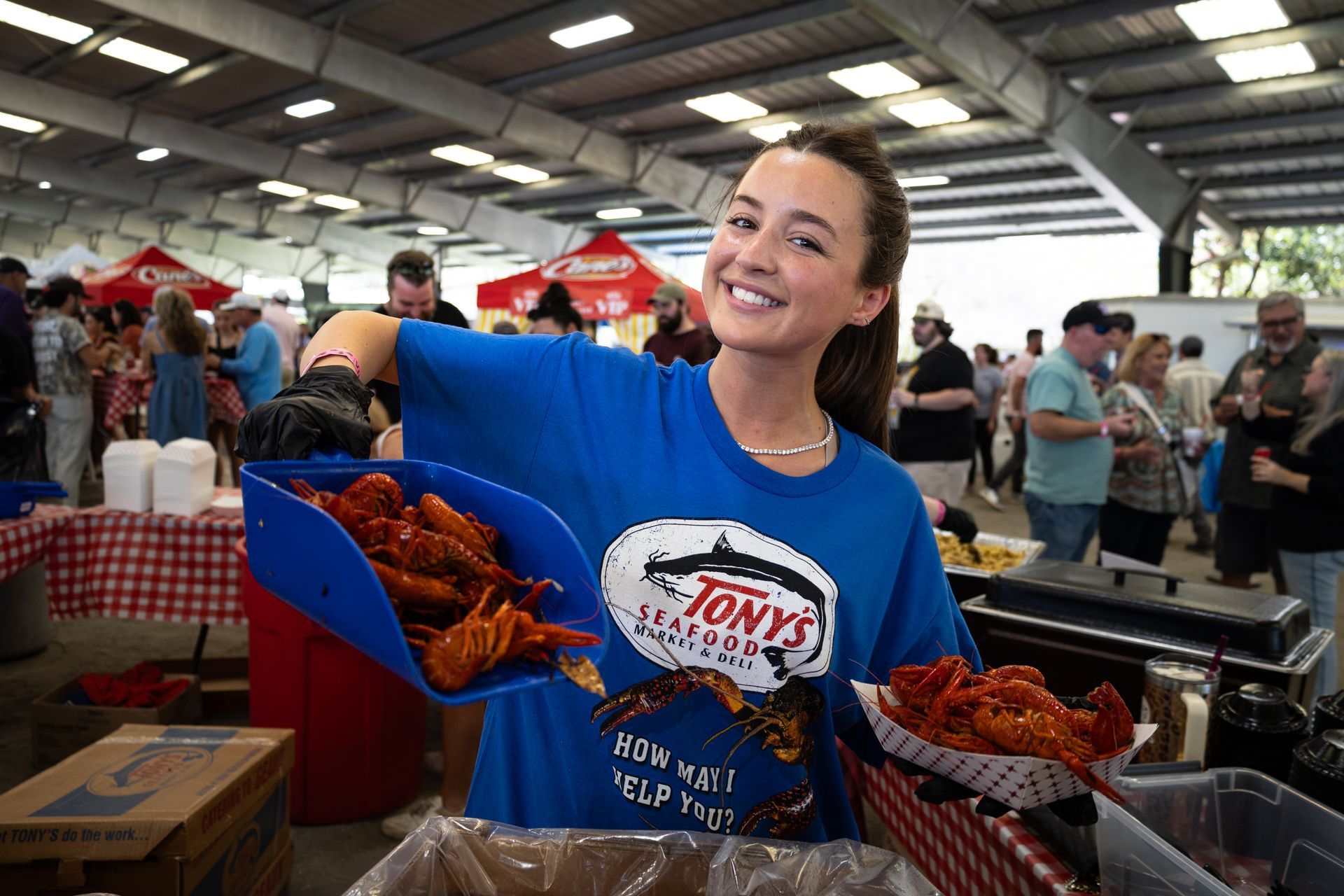 Smiling vendor holding trays of fried food at a busy indoor market stall