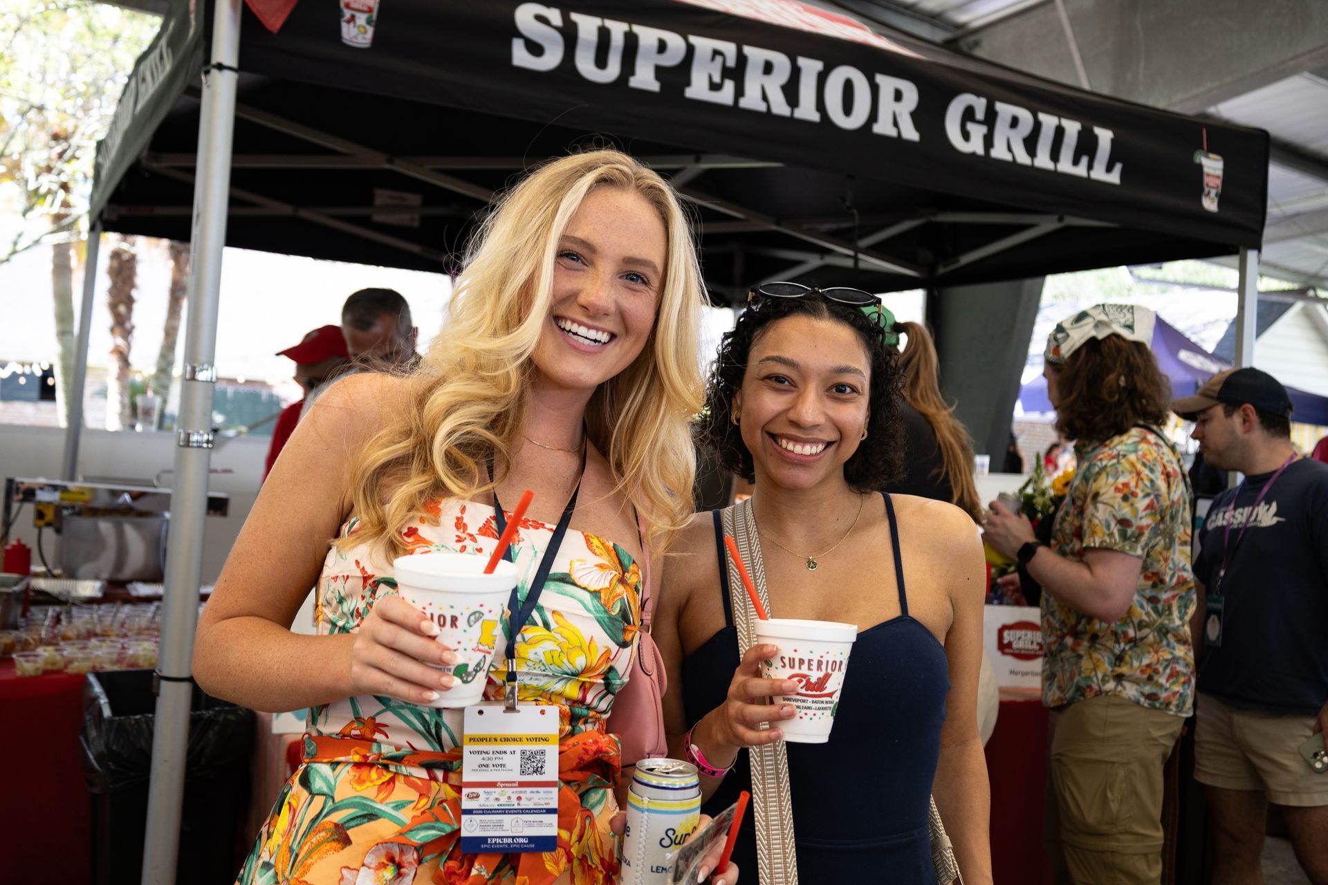 Two women smiling and holding drinks at a Superior Grill event booth