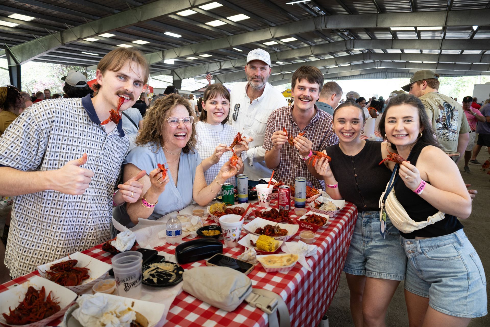 Group of people smiling around a market stall with red-and-white checkered tablecloth and food samples