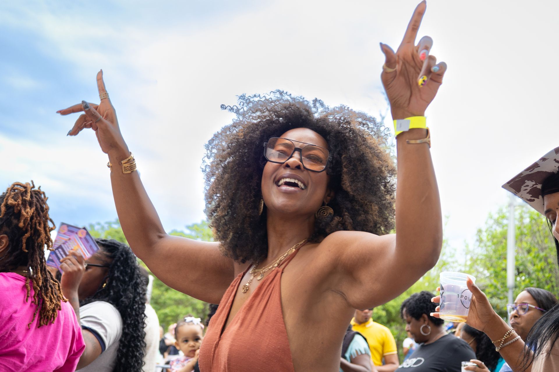 Person smiling and dancing at a lively outdoor festival, arms raised among a crowd