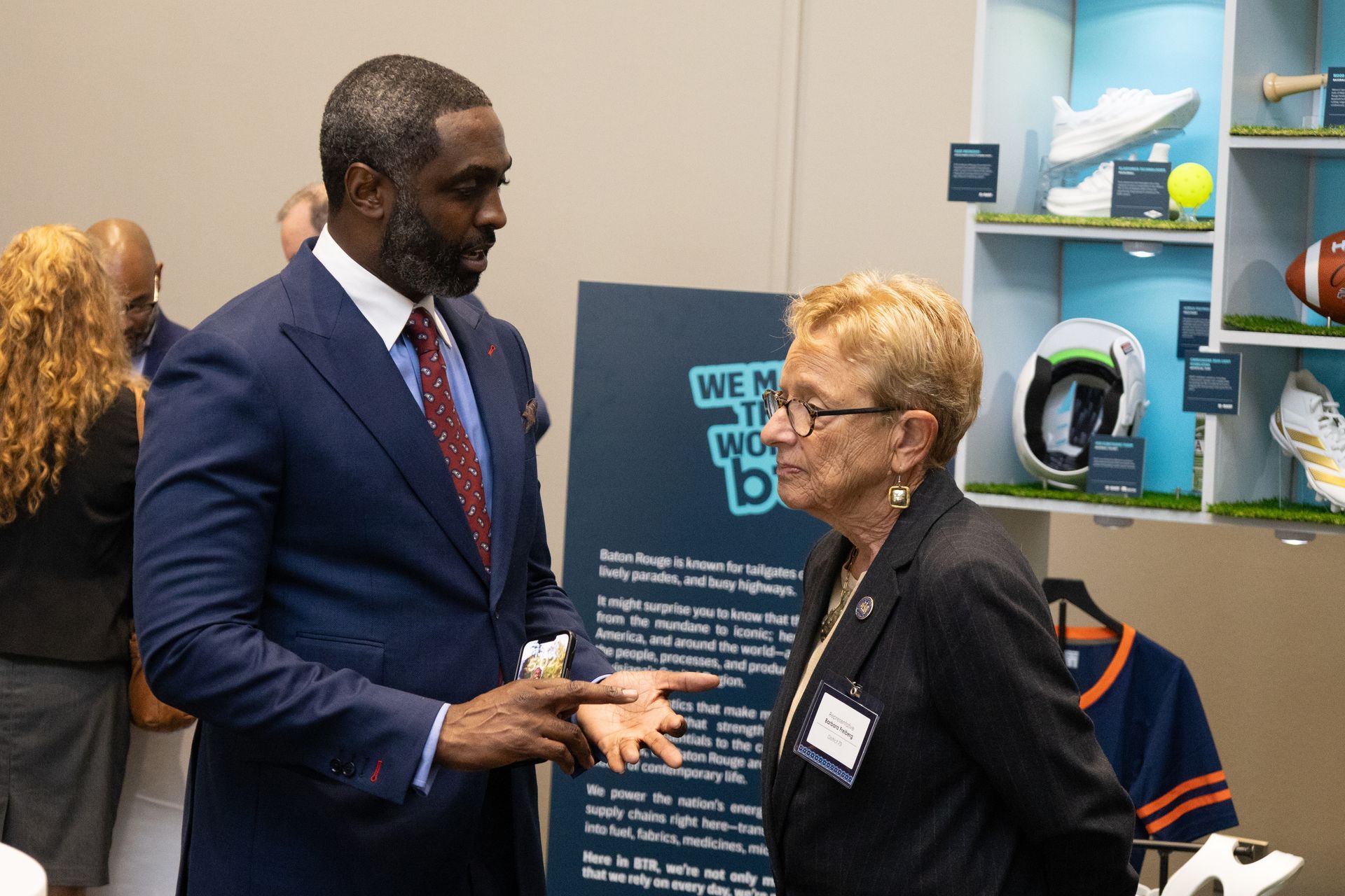 Two people conversing at a booth display, with pamphlets and a sign in the background.