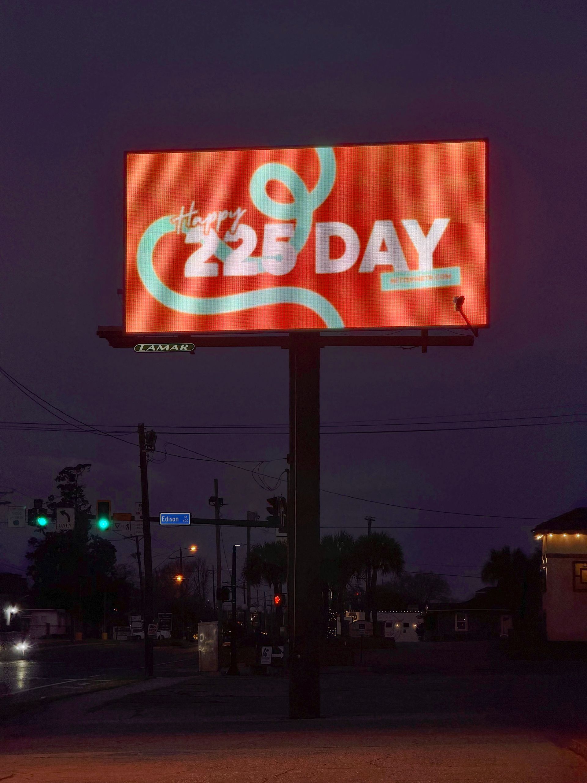 Red LED billboard reading “225 Day” at dusk above a street with traffic lights.