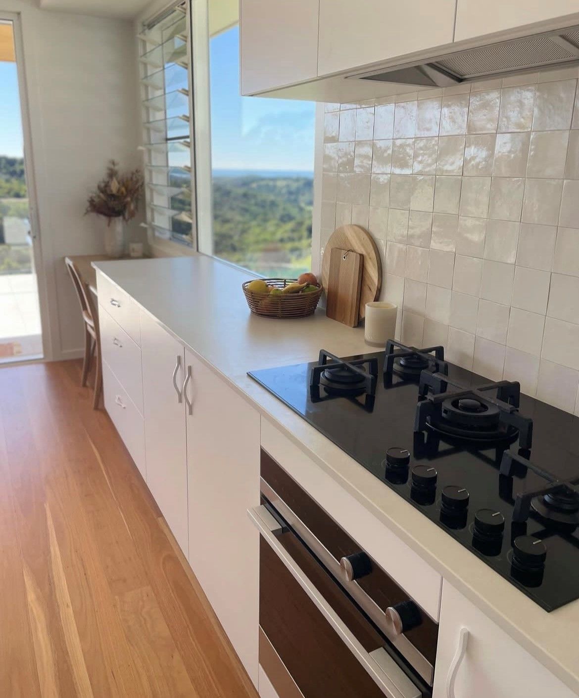 White modern kitchen with a cooktop, oven, and view through a window — Tile Trends in Tweed Heads South, NSW