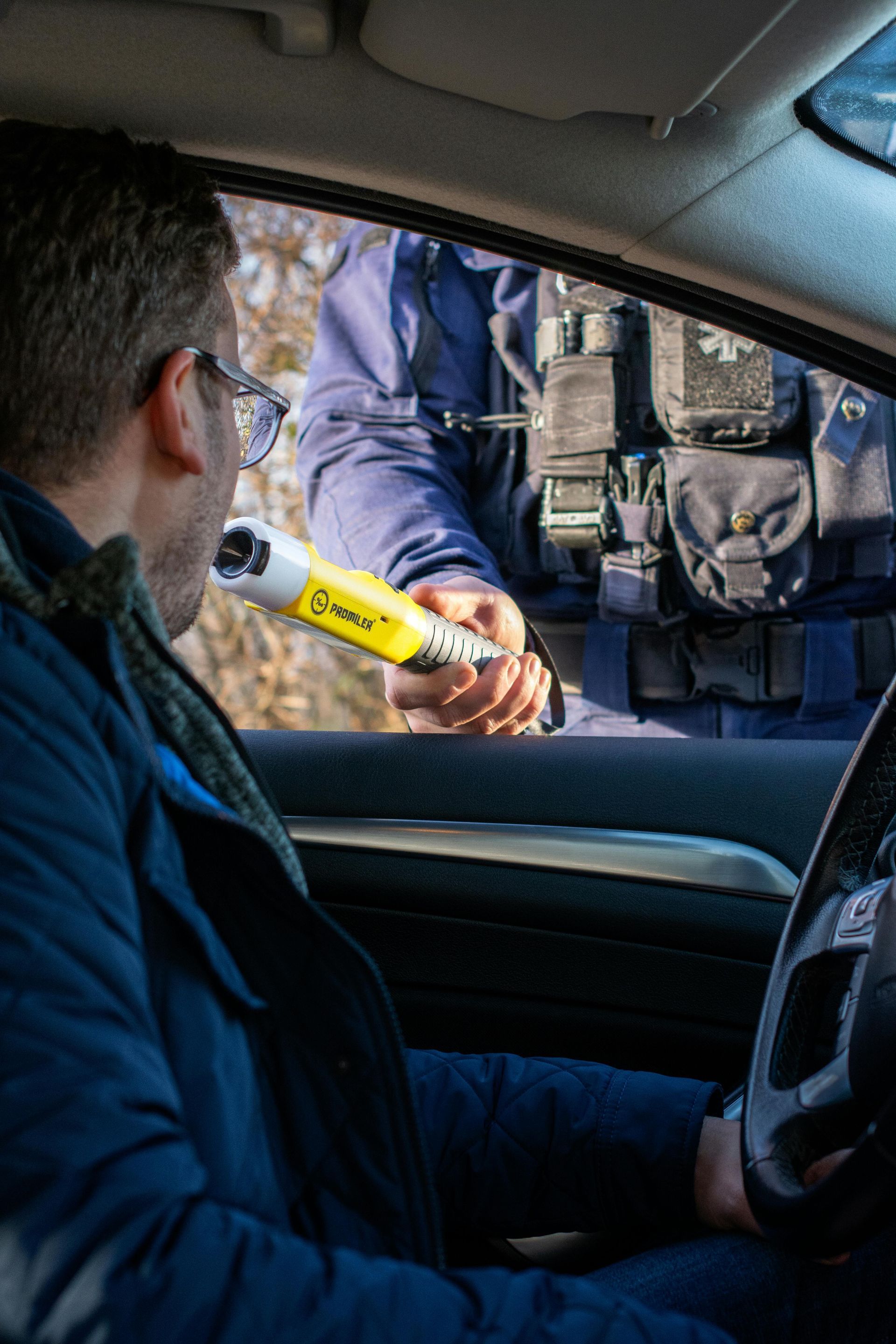 Driver in car hands yellow ID band to police officer at window, with another officer nearby.