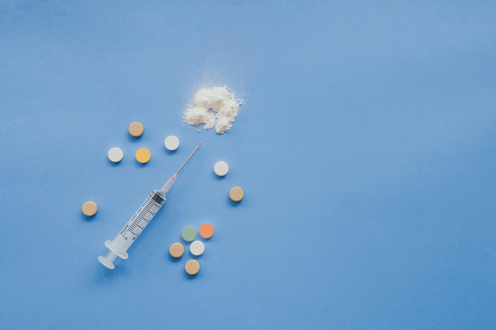 Syringe with scattered tablets and a white powder puff on a blue background