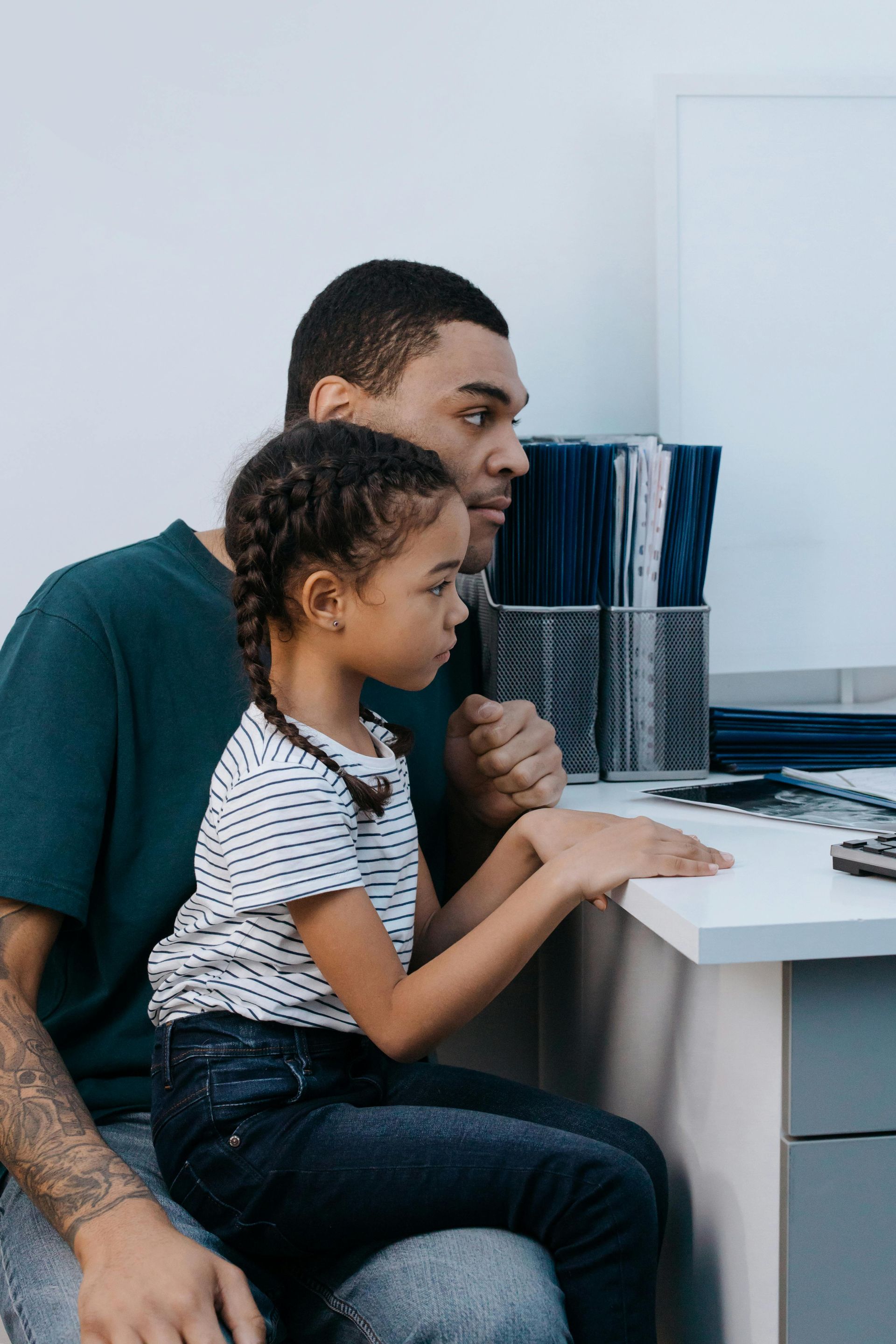 Adult and child seated at a desk, looking at a computer screen together