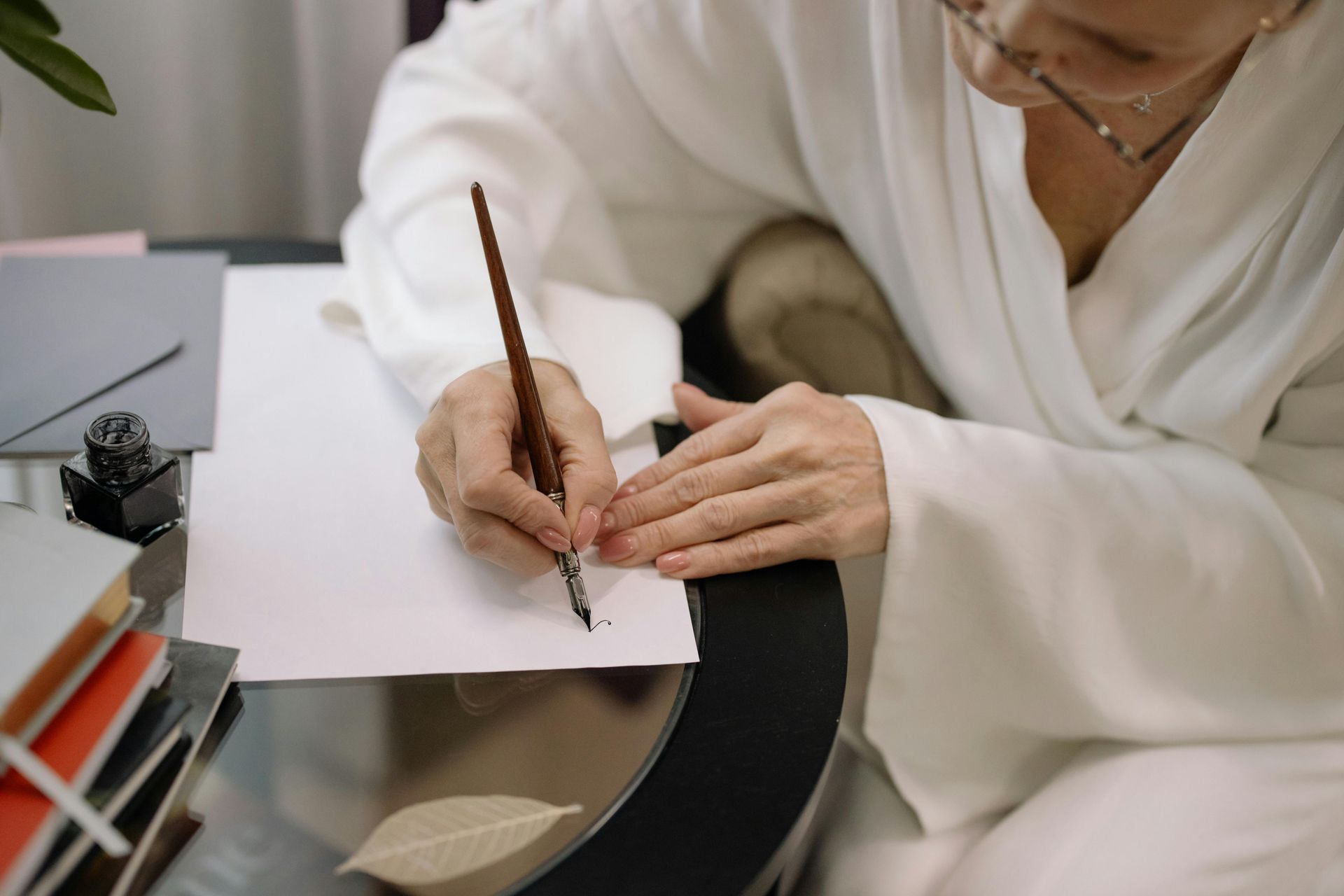 Person writing in a notebook at a desk, wearing a white robe, with books stacked nearby