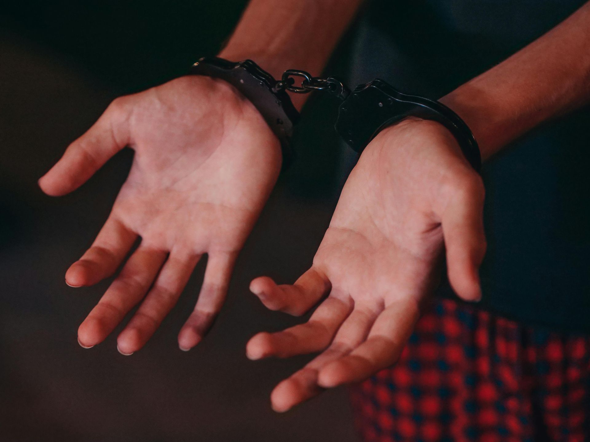 Hands cuffed with black handcuffs, palms up against a dark background.