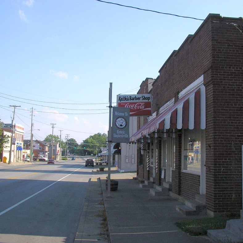 Street scene, brick buildings, barber shop sign, cars on road, clear sky.