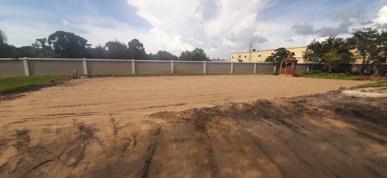 A dirt field with a fence and trees in the background.