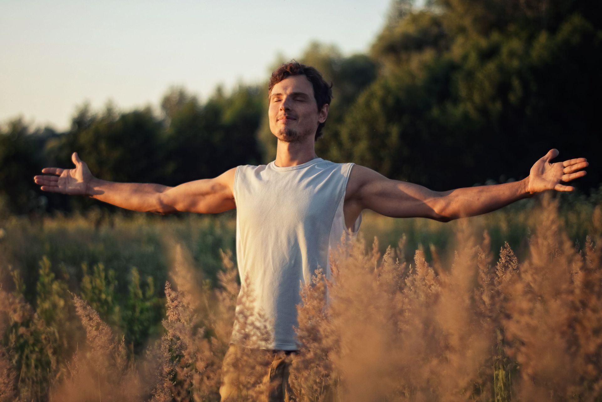 Person standing in a wildflower field with arms outstretched at sunset