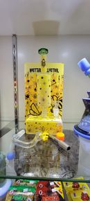 A yellow and black glass bong with a rectangular chamber, resting in a glass case.