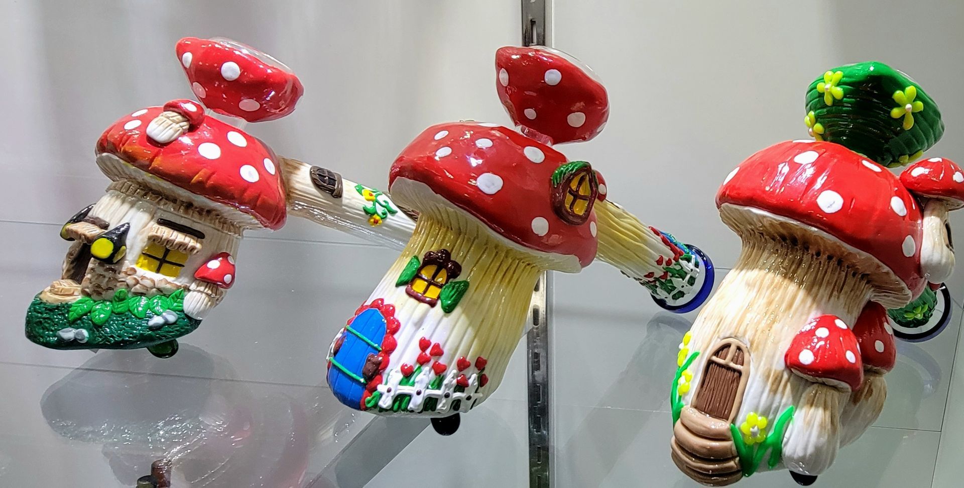 Three mushroom-shaped houses with red and white spotted caps, colorful doors and windows, on a shelf.