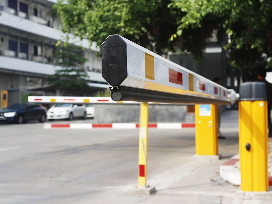 Parking barrier arm lowered across an entrance, with yellow control posts and blurred street traffic behind.