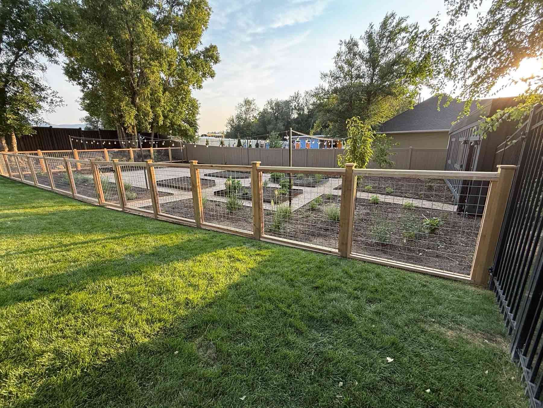 Backyard with wooden garden fence, grass lawn, and gravel area beside a house at sunset