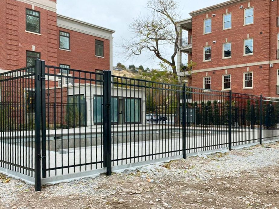 Snowy courtyard between red brick apartment buildings, bordered by a black metal fence.