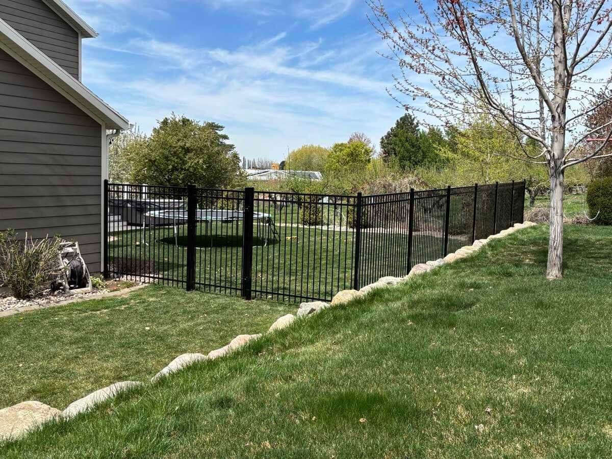 Black metal fence along a grassy yard beside a gray house on a sunny day
