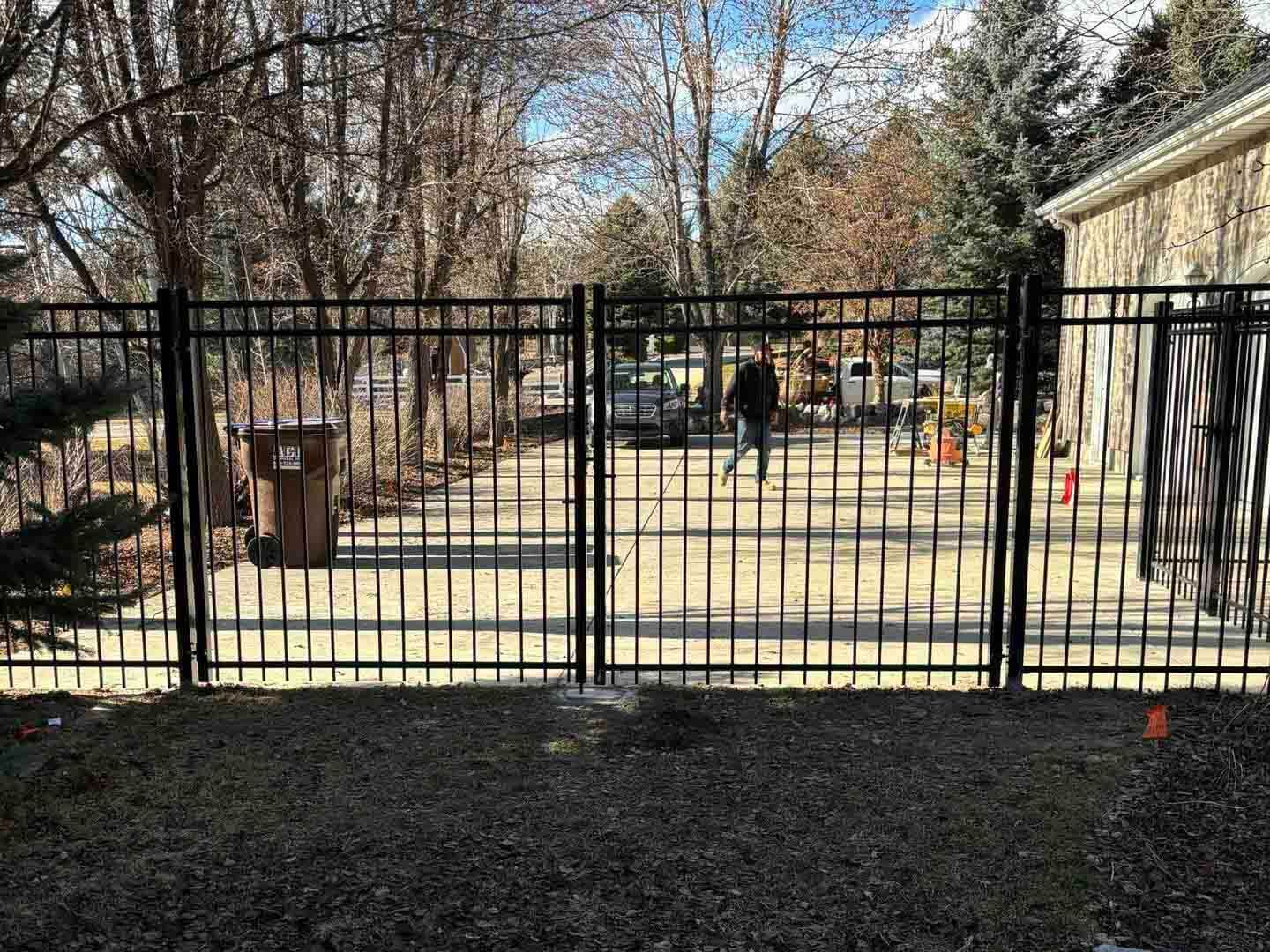 Black metal fence enclosing a sunlit backyard with trees, a playset, and a house on the right