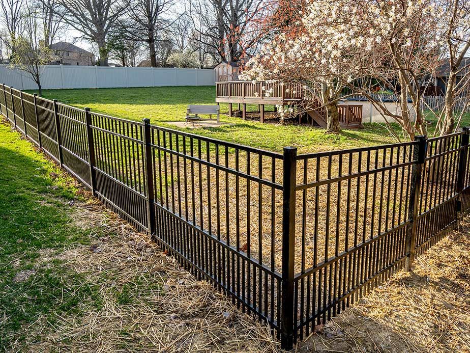 Black metal fence enclosing a grassy backyard with a wooden deck and blooming trees