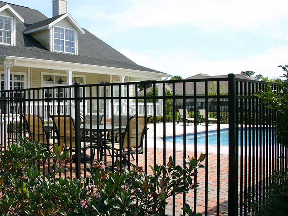 Backyard patio with black metal fence, chairs, and a swimming pool beside a house.