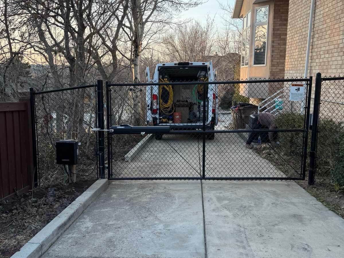 Open black chain-link gate in a driveway with a truck parked behind it