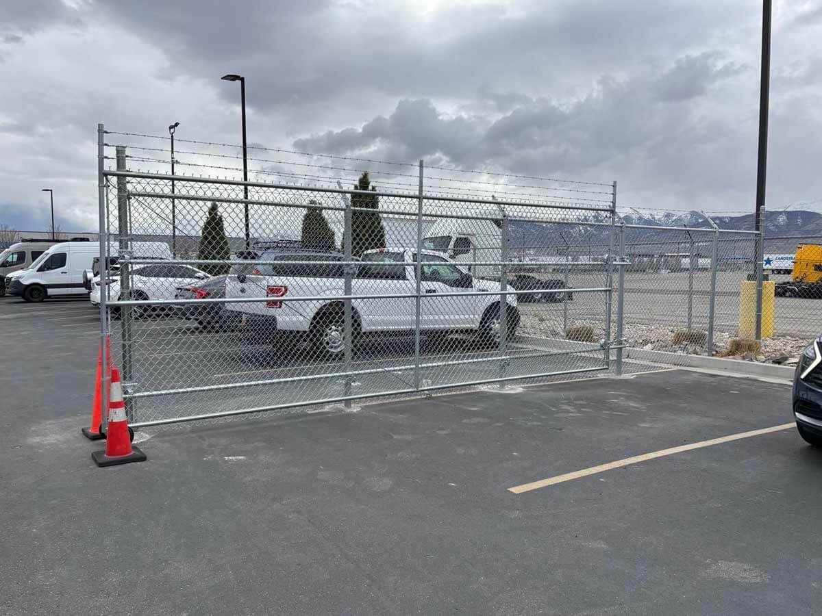 Chain-link fenced parking lot with white pickup trucks and orange traffic cones under a cloudy sky