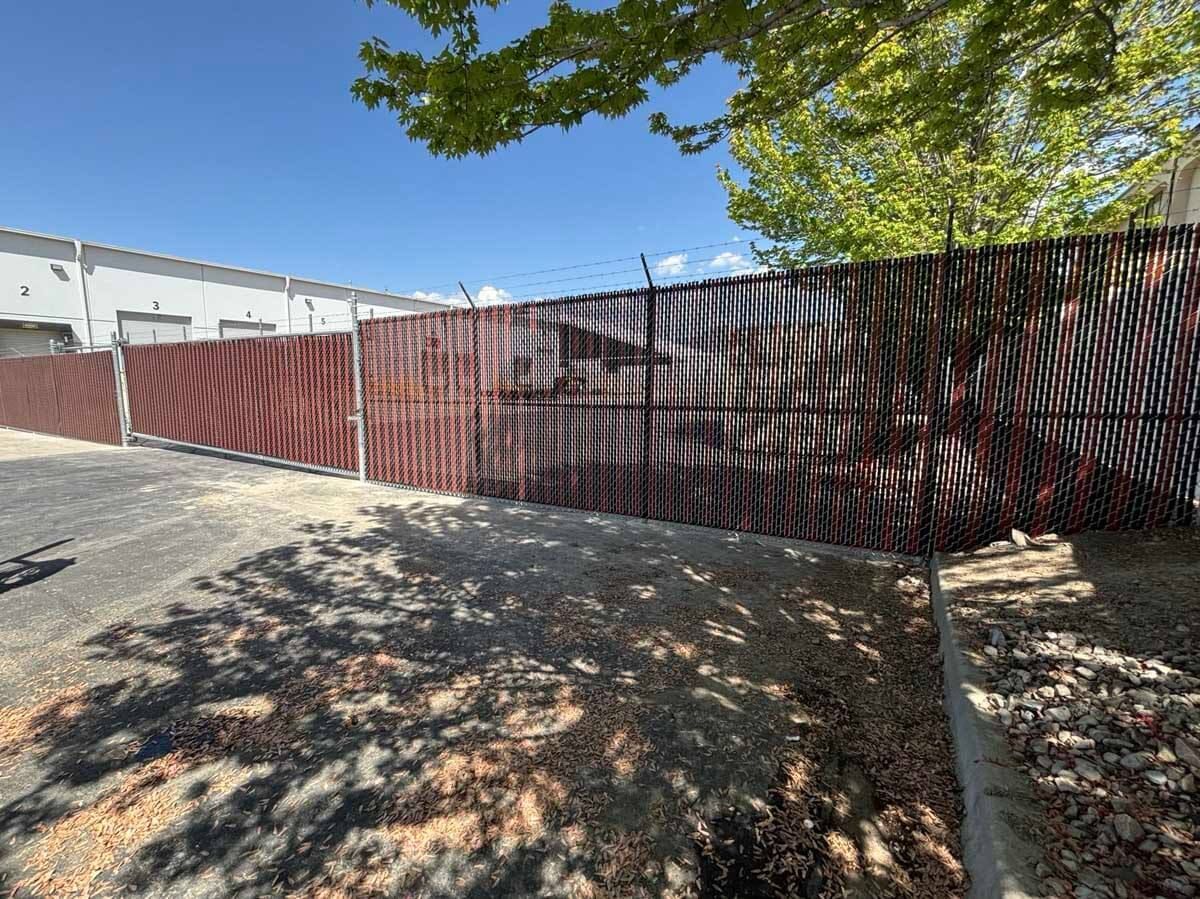 Red fence along a sloped driveway beside a white building under a clear blue sky.