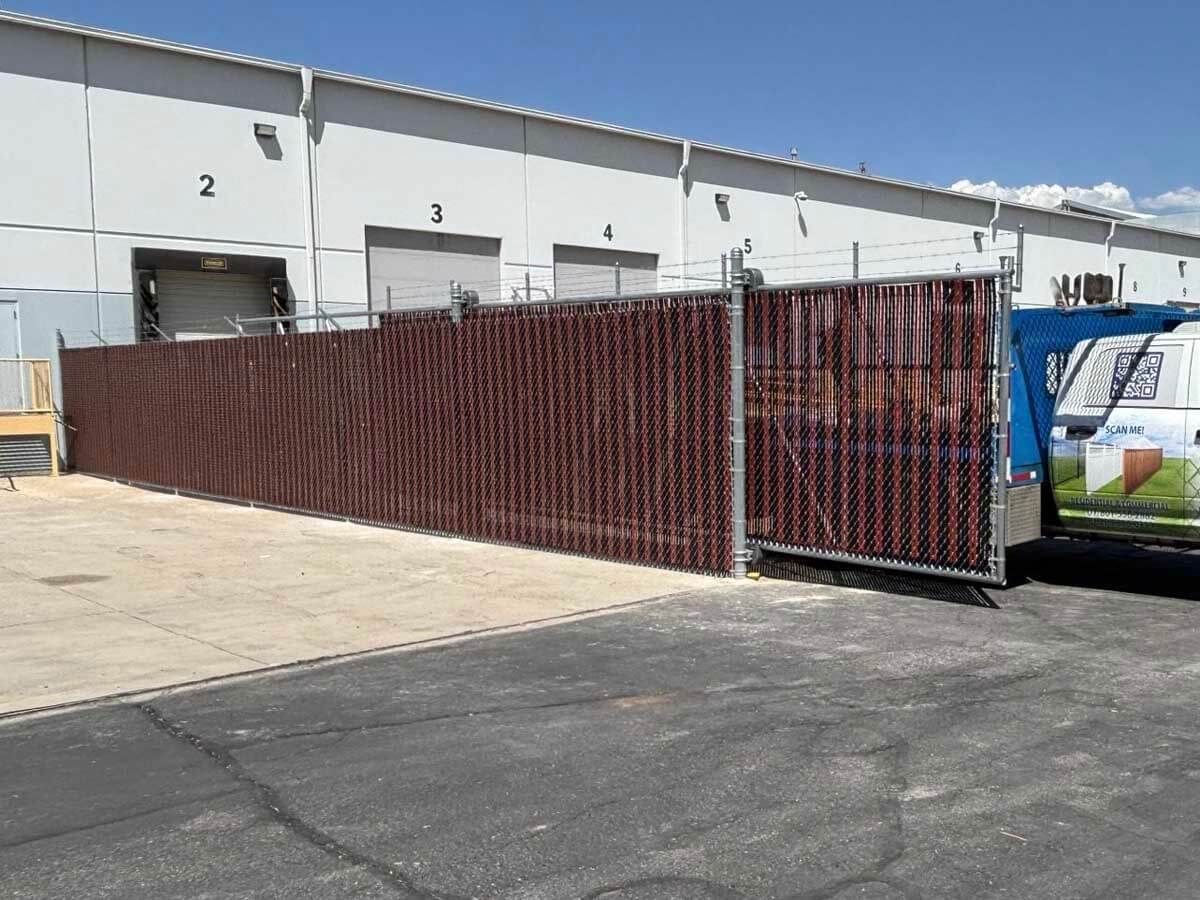 Red chain-link fence blocking warehouse loading bays, with a truck at the right edge.