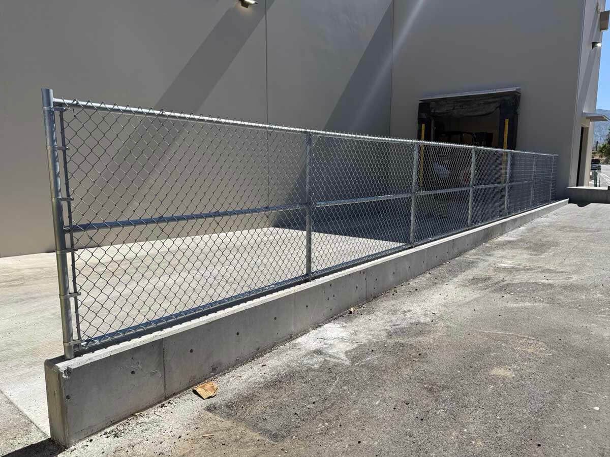 Chain-link fence along a concrete ramp beside a gray building