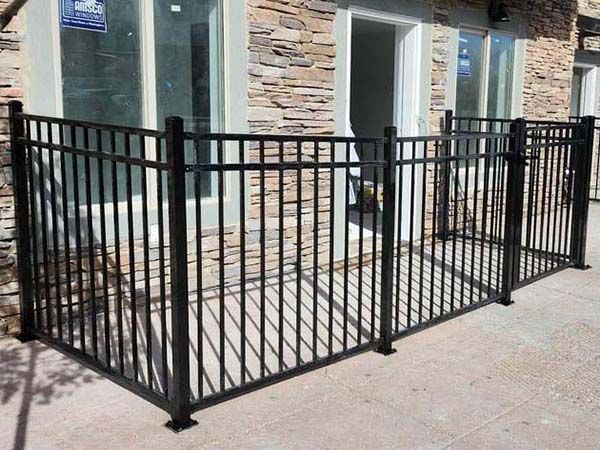 Black metal fence enclosing a small front patio beside a stone house with windows and a door
