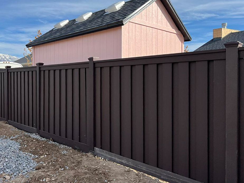 Dark brown metal fence along a gravel lot beside a pink house and blue sky