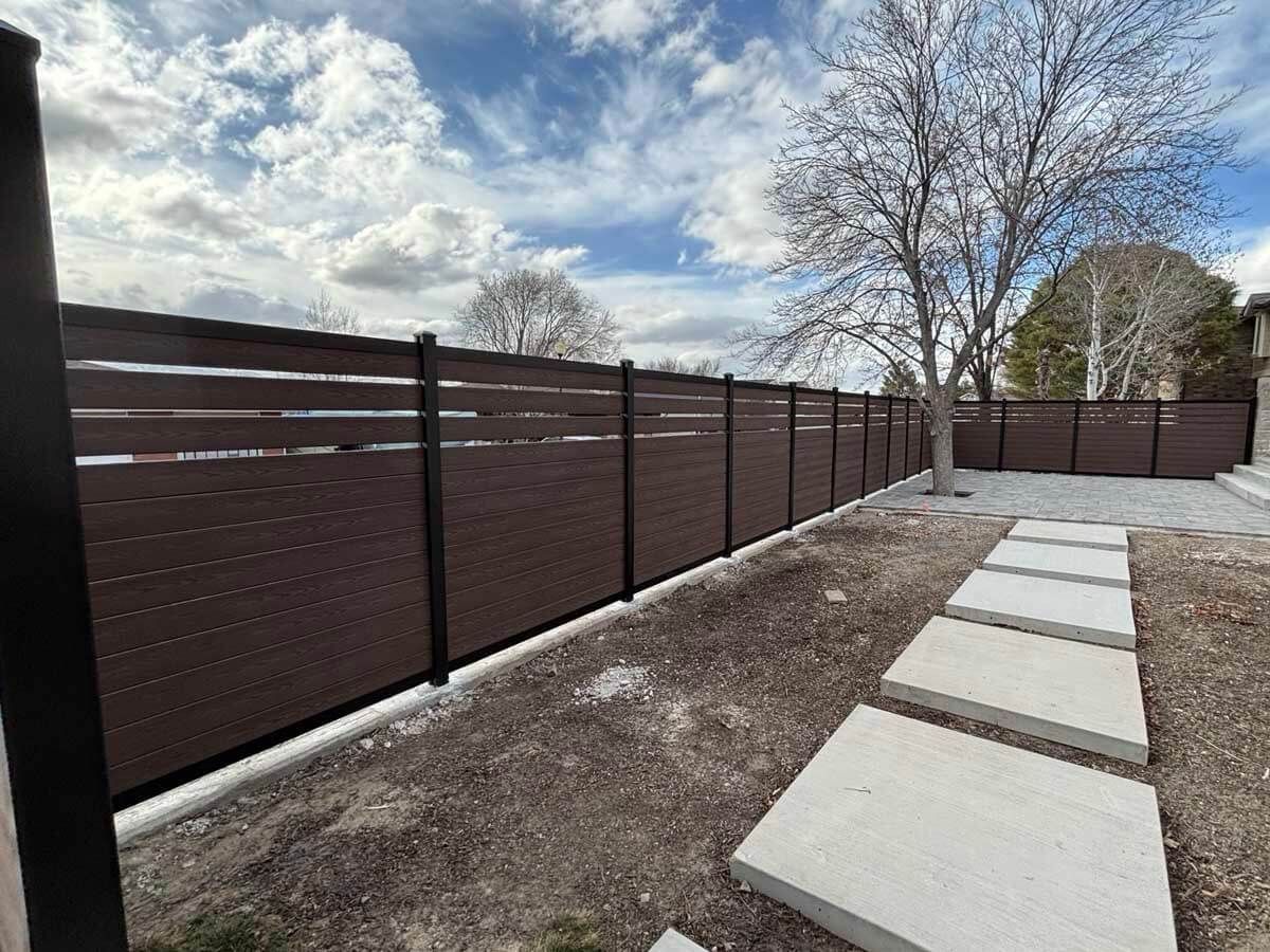 Backyard patio with concrete stepping stones beside a dark privacy fence under a cloudy sky