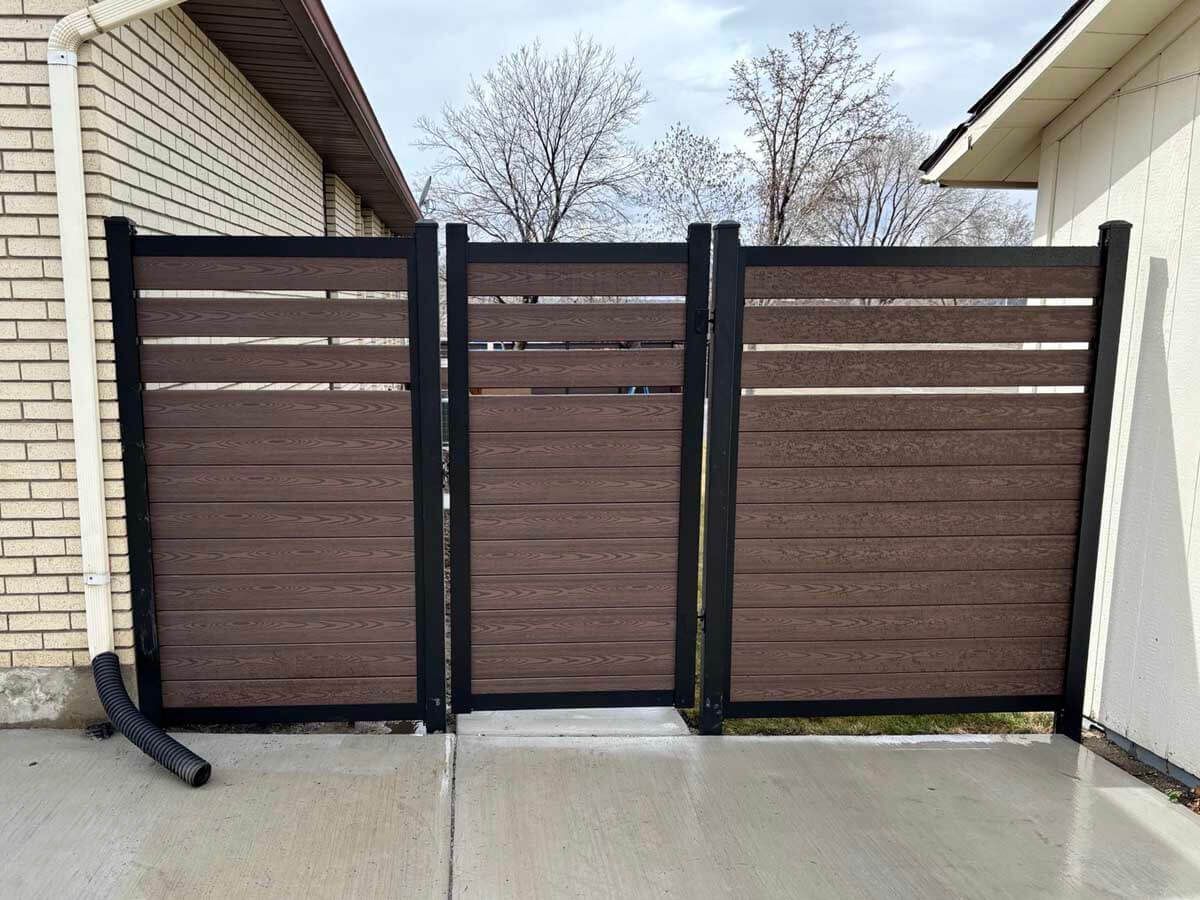 Closed brown slatted gate between brick and white buildings in a driveway