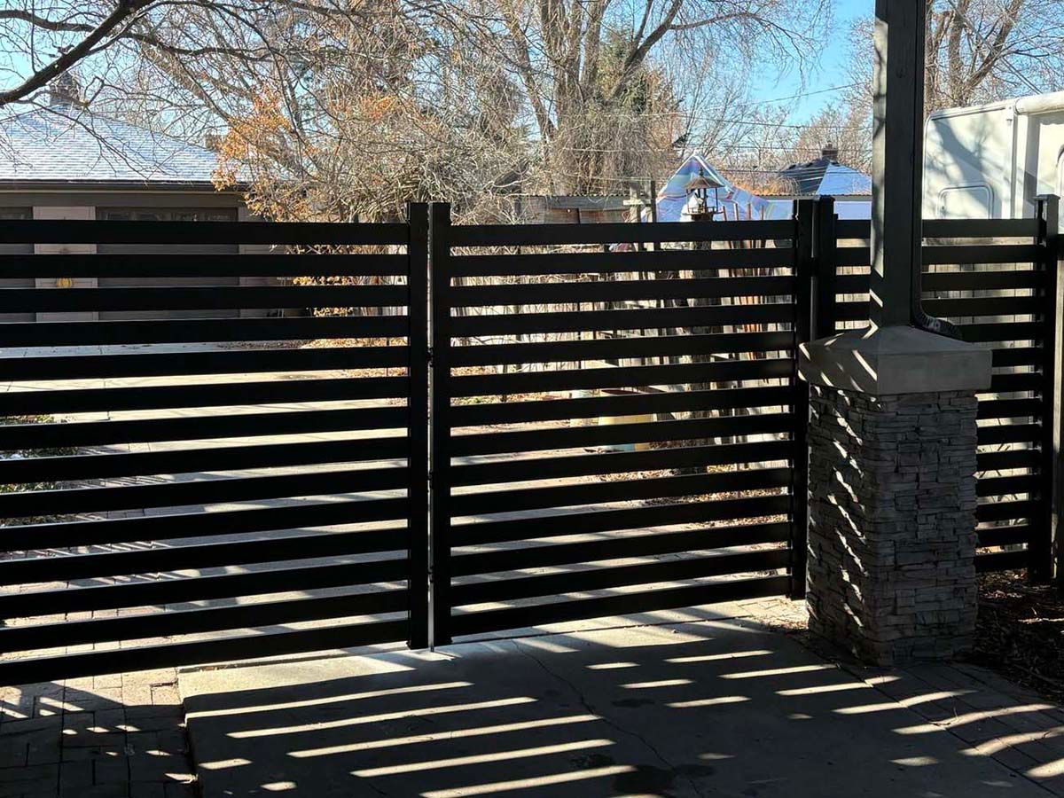 Black slatted gate and stone pillar blocking a driveway in bright sunlight