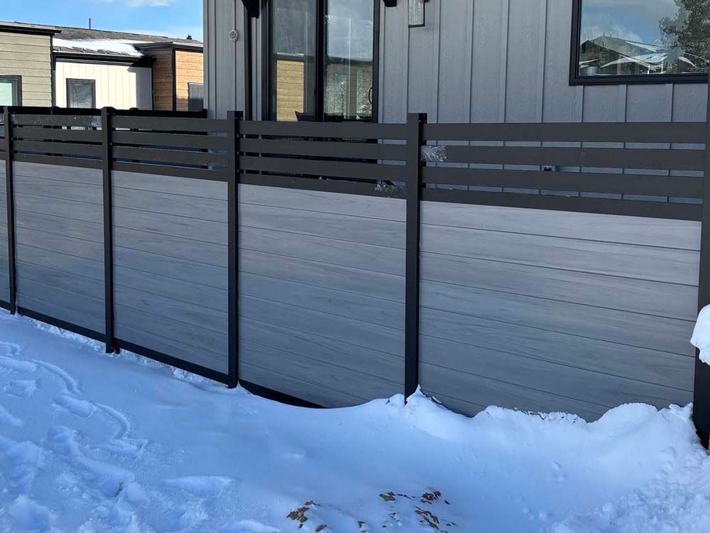 Snow-covered yard with a modern gray metal fence beside a house.