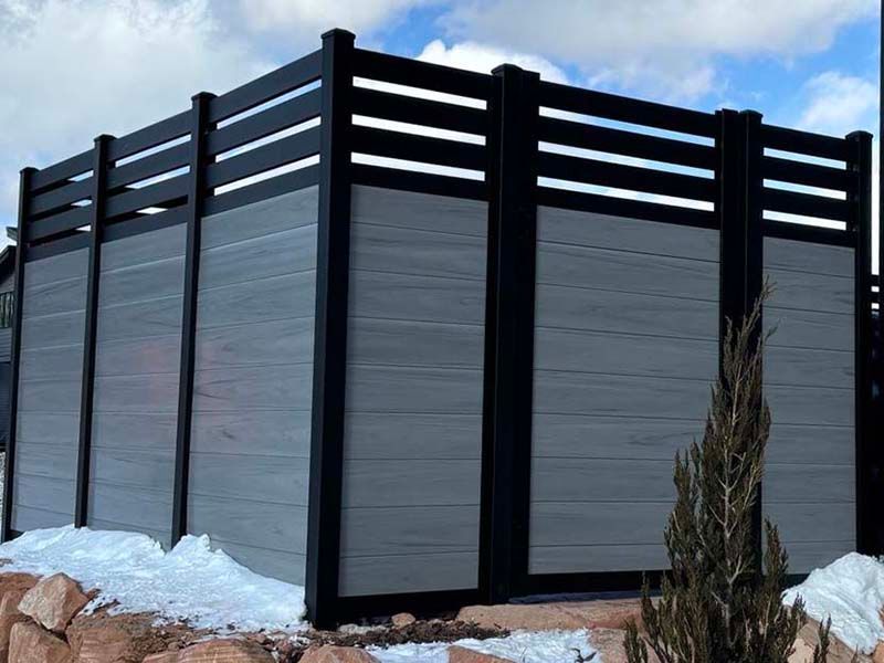 Black privacy fence with gray panels on a snowy outdoor property under a blue sky