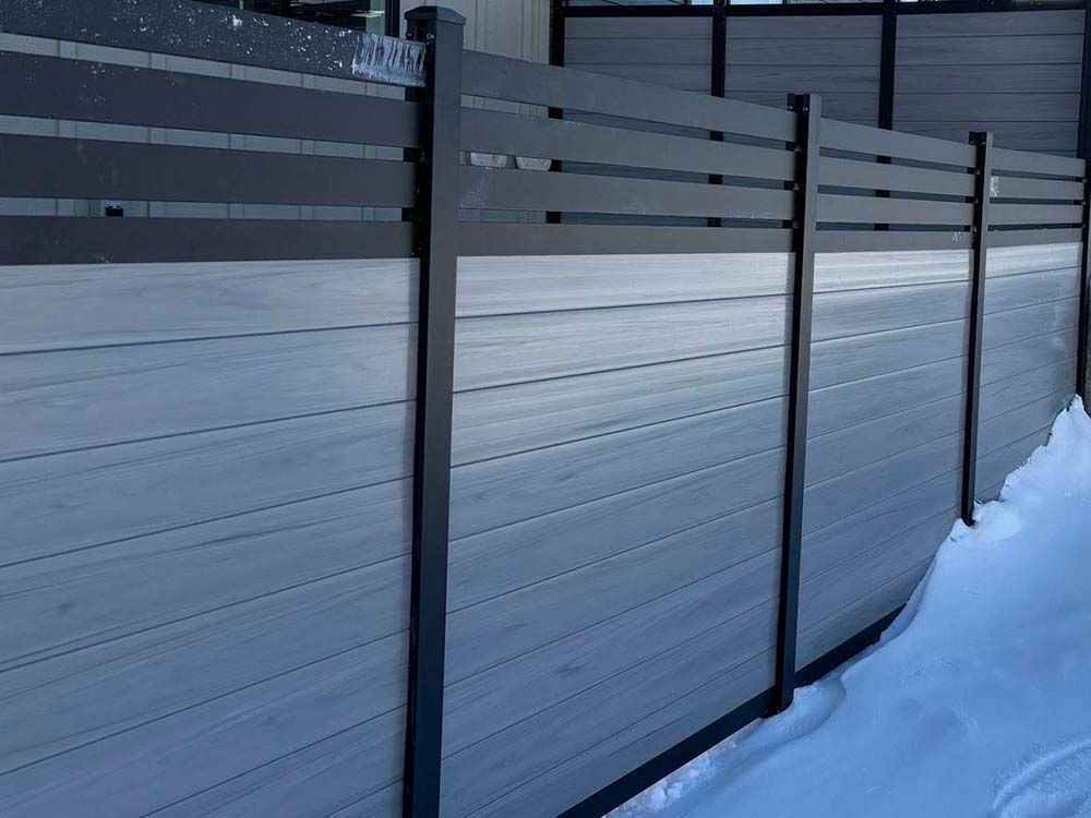 Snow-covered modern fence with dark posts and frosted panels along a walkway