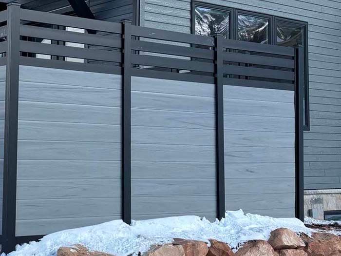 Modern gray privacy fence with black posts and slatted top, set beside a snow-covered ground.