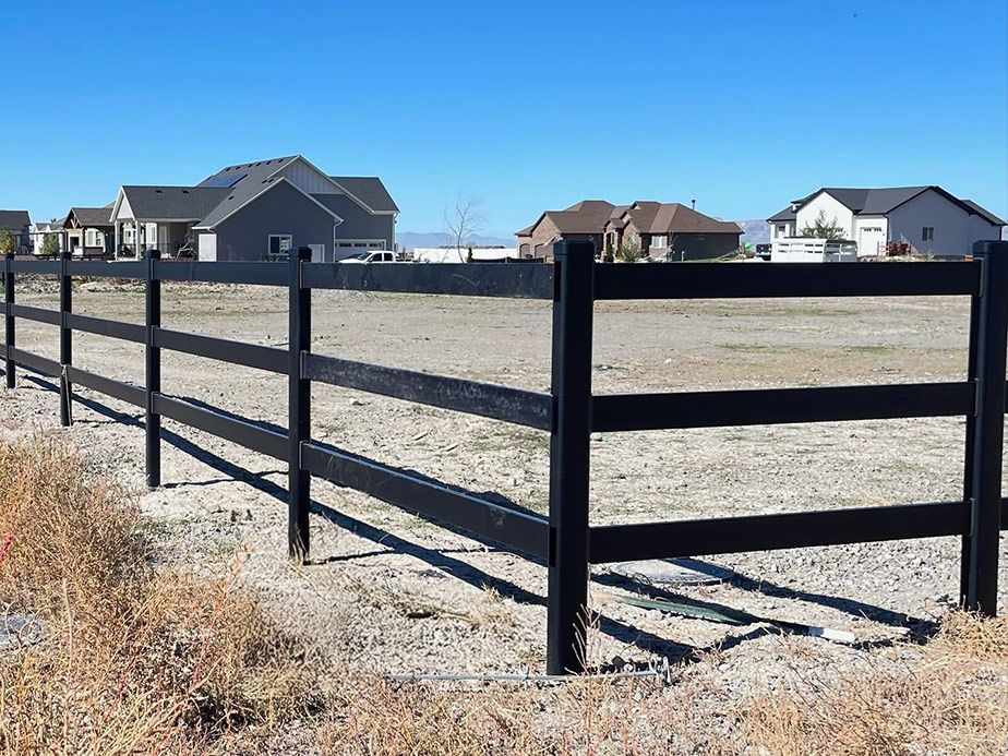 Black wooden fence around an empty dirt lot in a suburban neighborhood under a clear blue sky
