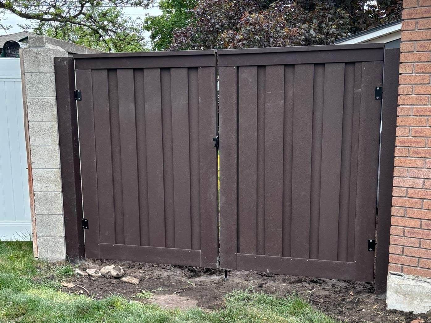 Closed brown wooden double gate between a stone wall and brick pillar outdoors