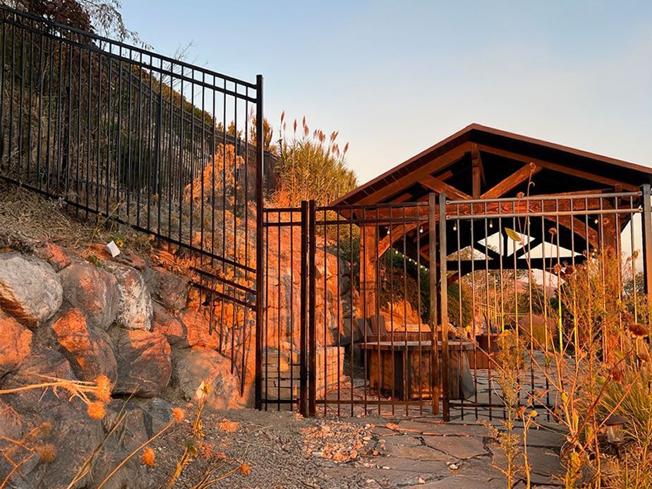 Iron gate and stone wall beside a wooden gatehouse in a dry, sunlit yard