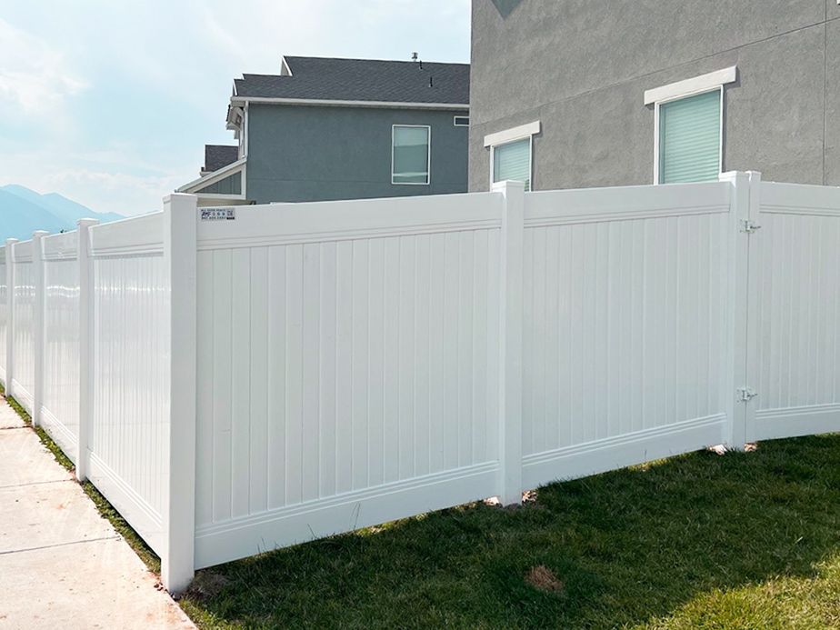 White vinyl fence along a sidewalk beside a gray house and green grass