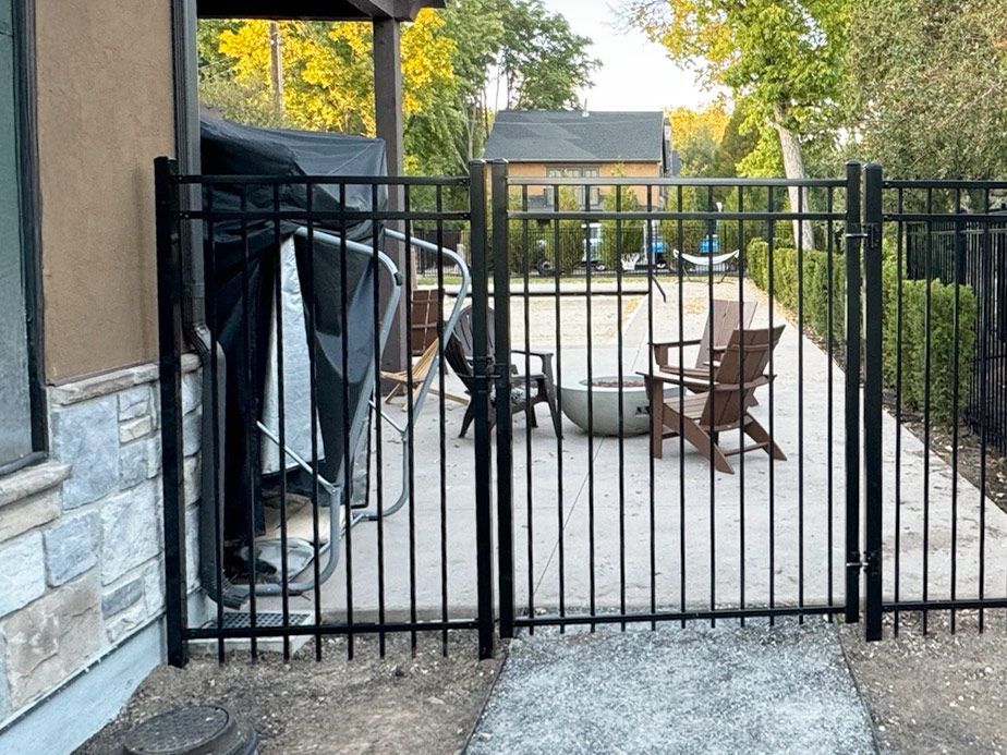 Patio with black metal gate, covered grill, and two brown chairs on a concrete terrace