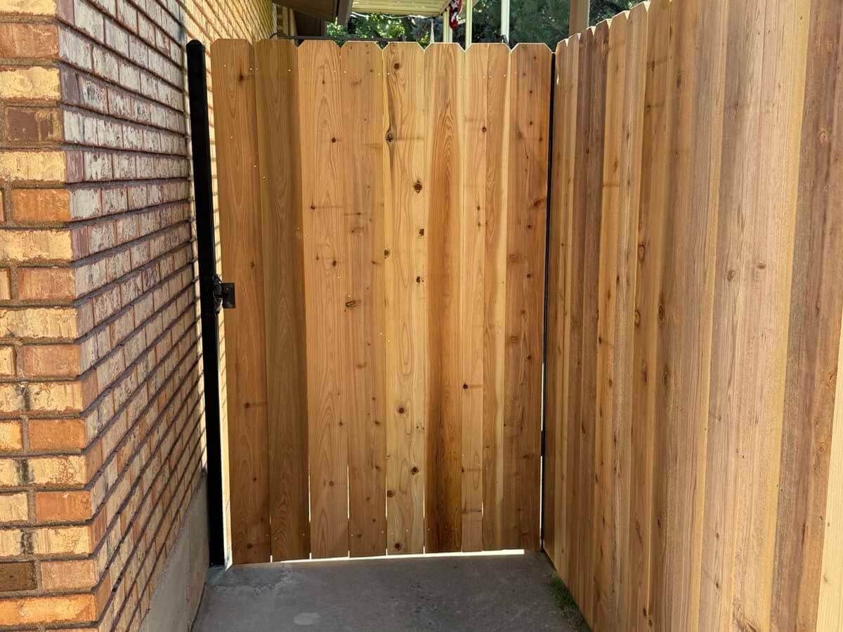 Wooden double garden gate with one door open and one closed, showing black hinges and latch.
