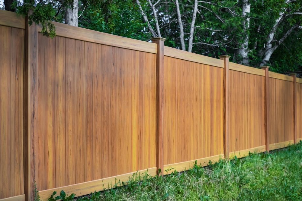 Wooden privacy fence with tan trim along a grassy yard, backed by trees
