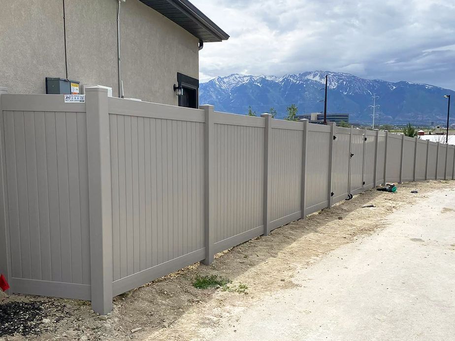 Gray metal fence along a dirt road beside a house, with snowy mountains in the background