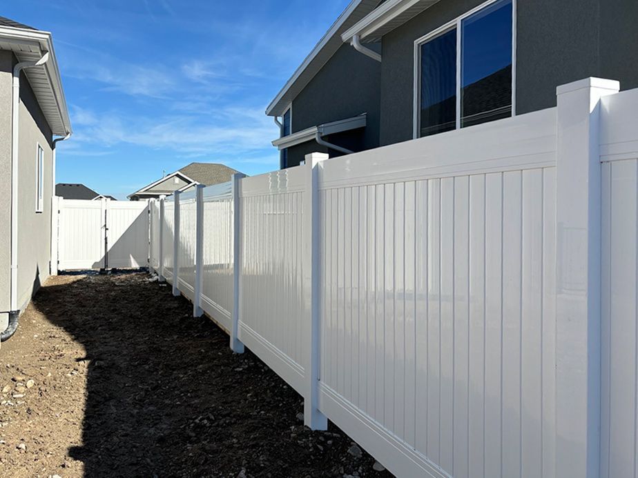 Narrow side yard with white vinyl fence between houses under a blue sky