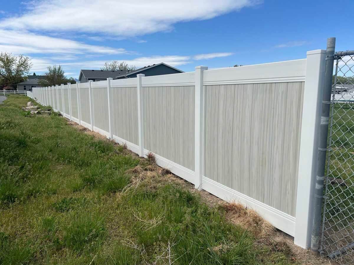 White vinyl privacy fence along a grassy roadside under a cloudy sky