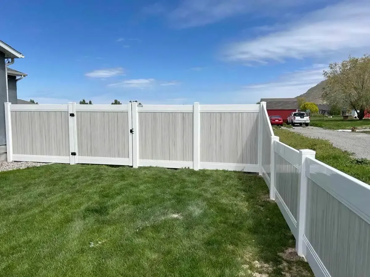 White vinyl fence around a green lawn under a blue sky, with a driveway and red truck in the background