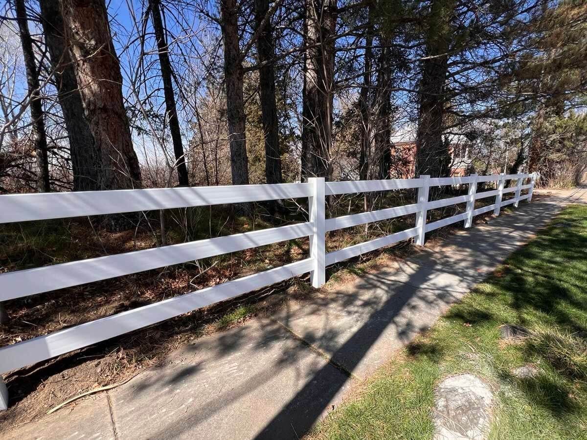 White fence along a wooded path with long shadows in bright sunlight